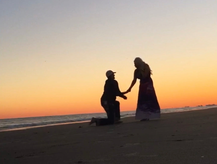 photo of a couple on a beach at sunset, with the man down on one knee proposing to his girlfriend